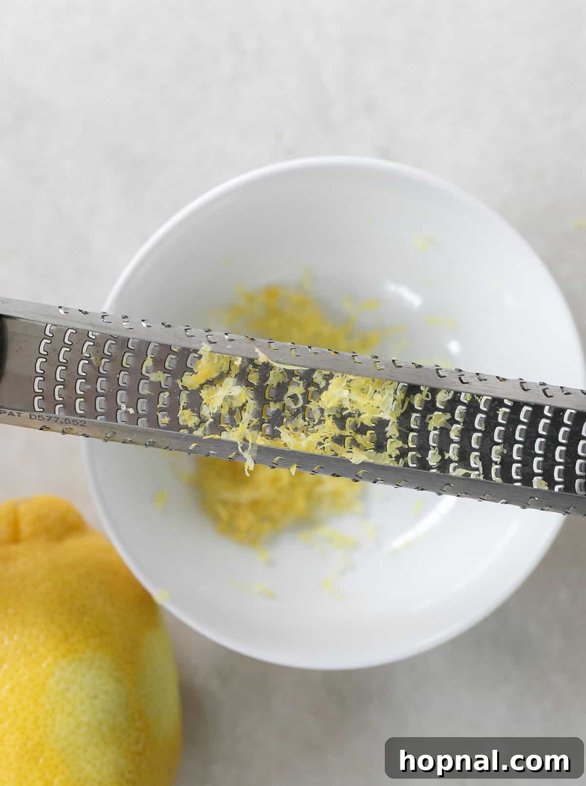 A bowl of fresh lemon zest with a zester resting beside it, highlighting the vibrant color and texture.