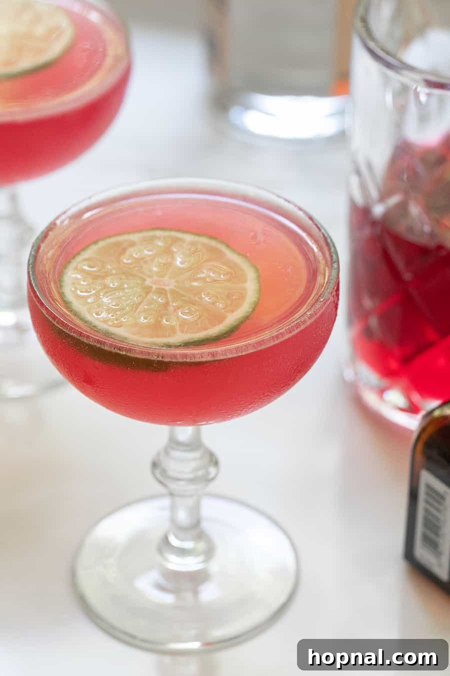 Blush & Sip 19 Pink cosmopolitan cocktail recipe with a lime slice.