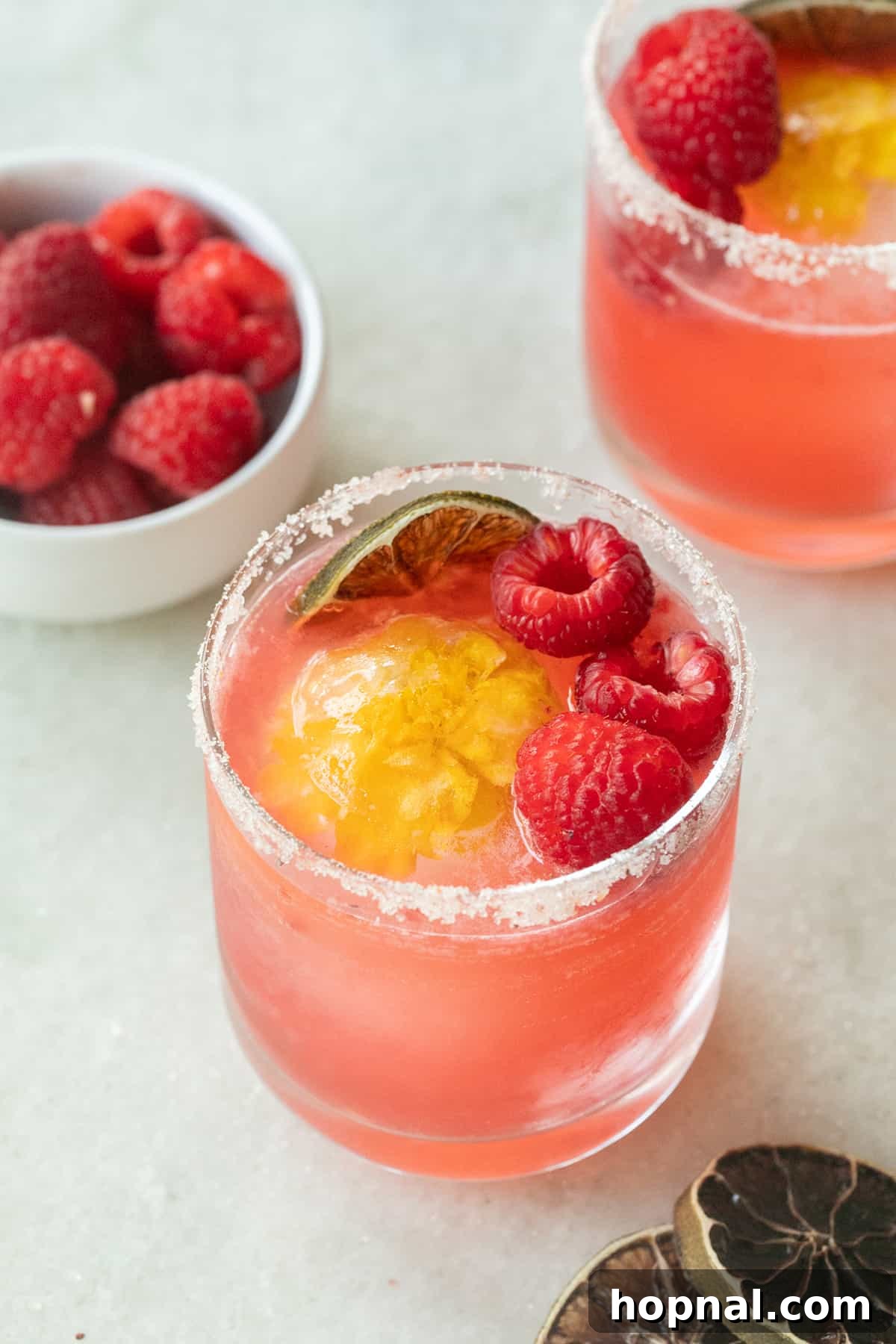 Blush & Sip 7 Raspberry margarita on the rocks with an edible flower ice cube and fresh raspberries.
