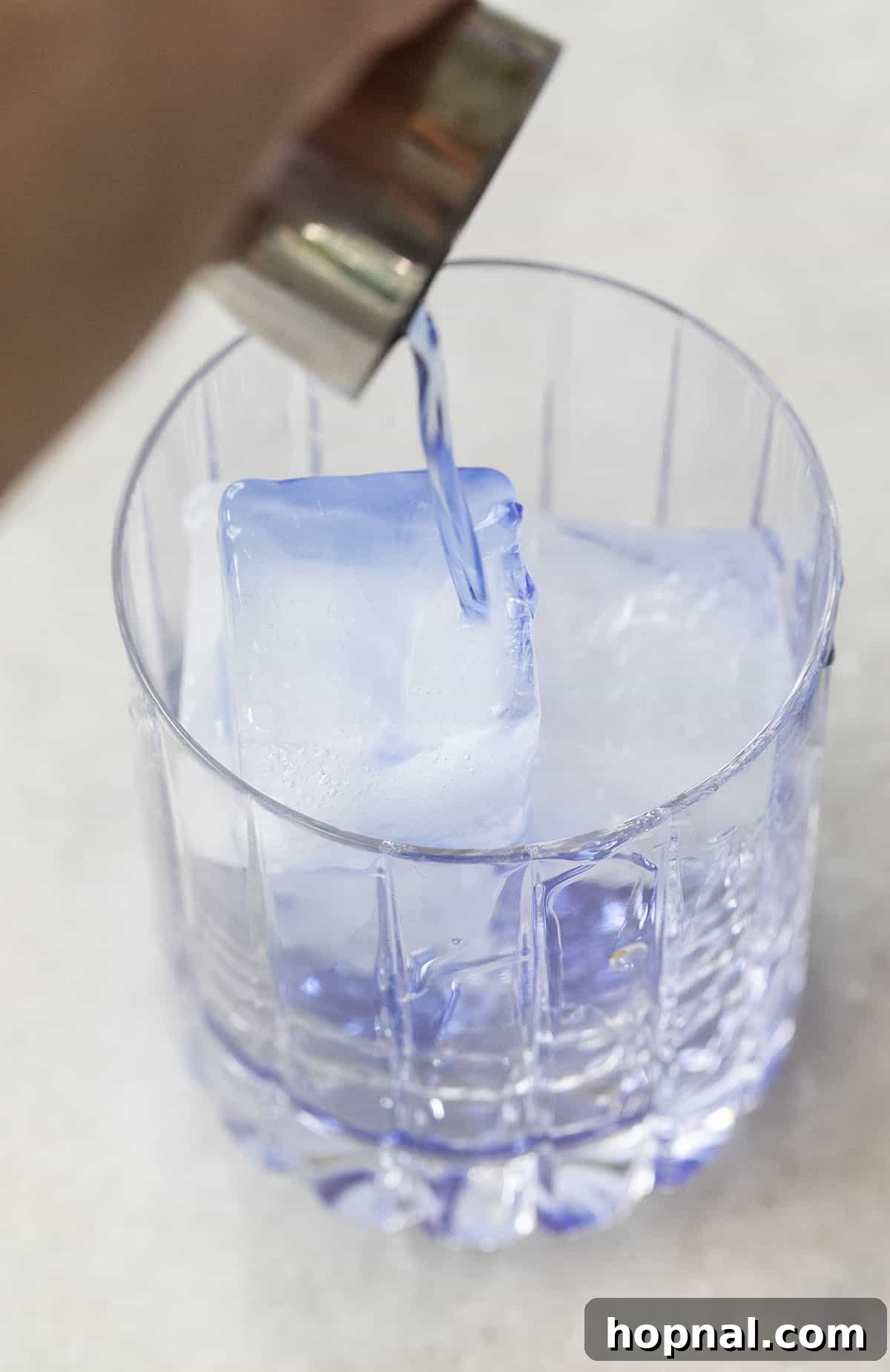 A close-up of Empress Gin being poured into a glass filled with ice, illustrating its deep blue color before mixing.