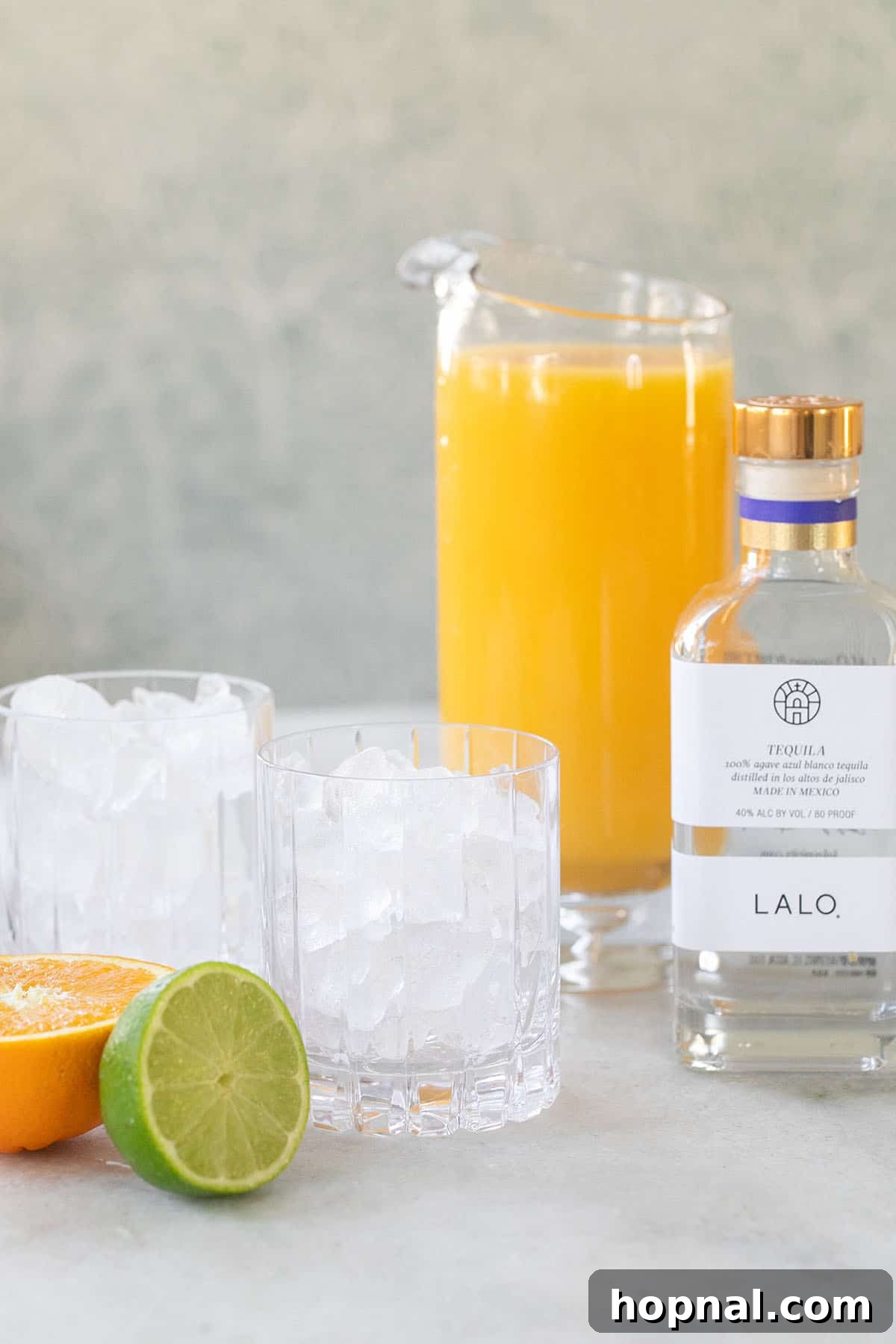 Essential ingredients for a Tequila and Orange Juice cocktail: a glass with ice, a bottle of tequila, a fresh lime, and a jug of orange juice.