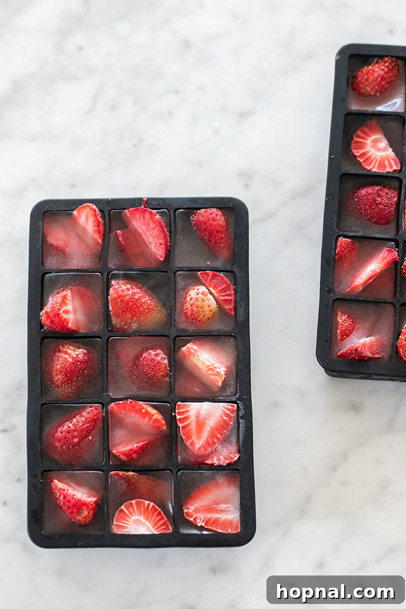 Strawberry ice cubes partially frozen in an ice cube tray, showcasing the fruit.