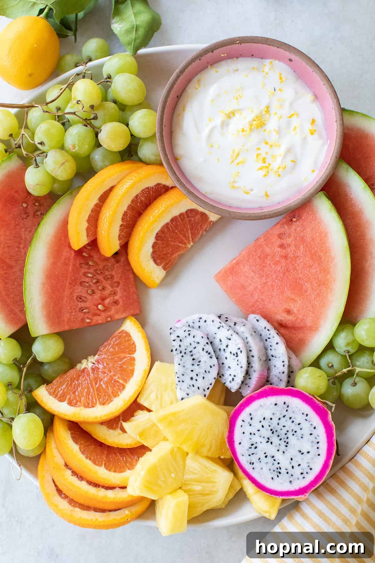 A vibrant fruit platter featuring neatly sliced watermelon, bright orange segments, and creamy fruit dip in a bowl.