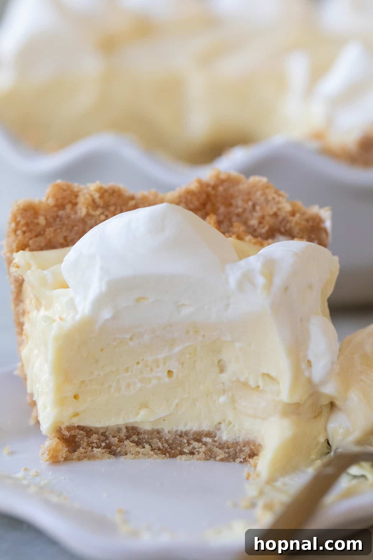 A tantalizing slice of banana pie with a thick, golden graham cracker crust, drizzled with caramel and whipped cream.