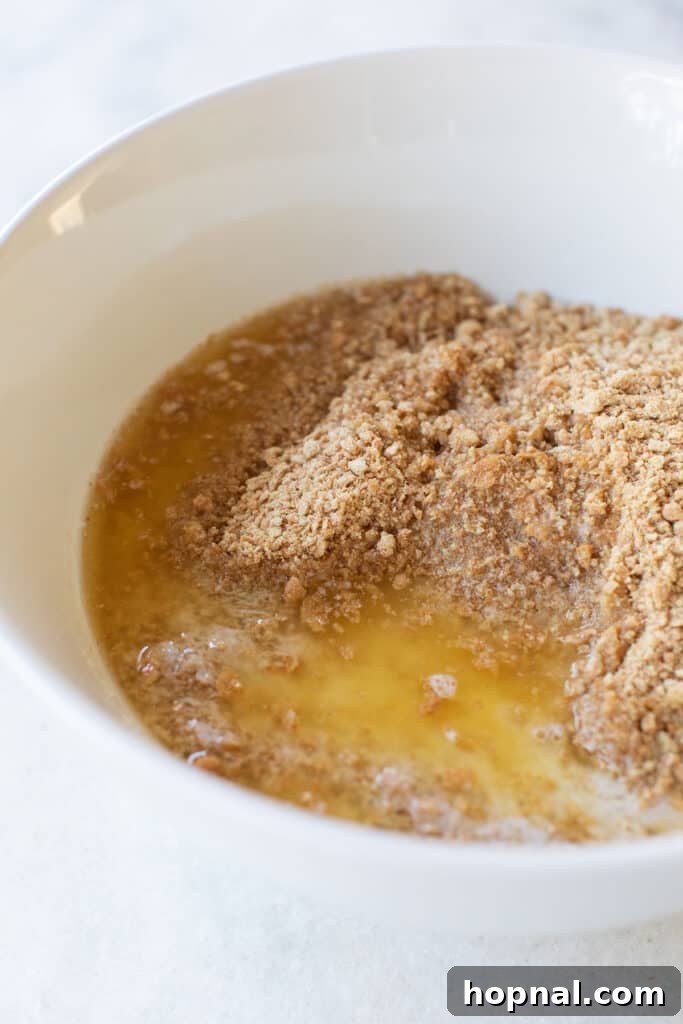 A clear glass bowl showcasing the golden graham cracker crust mixture, perfectly moistened and ready for pressing.