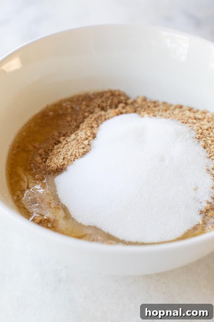 A bowl filled with the graham cracker crumb mixture, including visible bits of butter, sugar, and salt, being prepared for pressing.