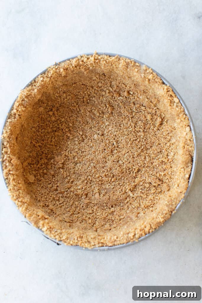 The graham cracker crust mixture pressed firmly into a springform pan, creating a smooth and even base.