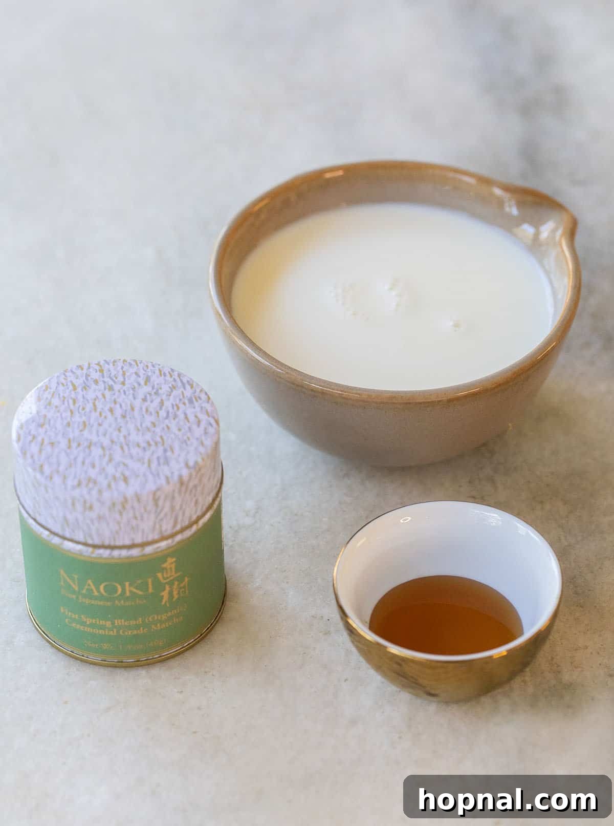 A visual display of the simple ingredients needed for an iced matcha latte: high-quality matcha powder, a bottle of milk, and a jar of honey.