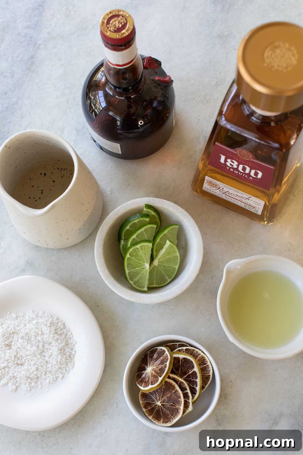 ingredients for a golden margarita laid out: gold tequila, fresh limes, simple syrup, and Grand Marnier