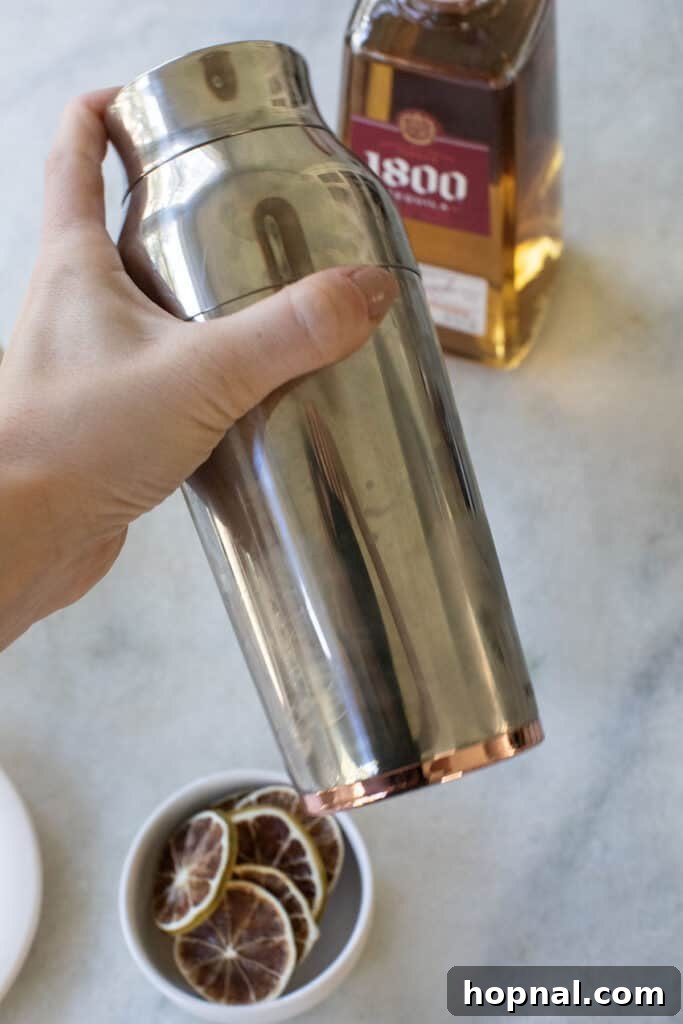 Shaking a golden margarita with ice in a metal cocktail shaker.