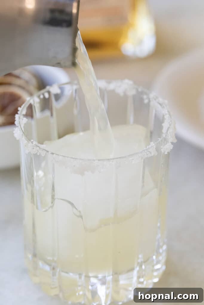Pouring a freshly shaken margarita over ice into a prepared glass.