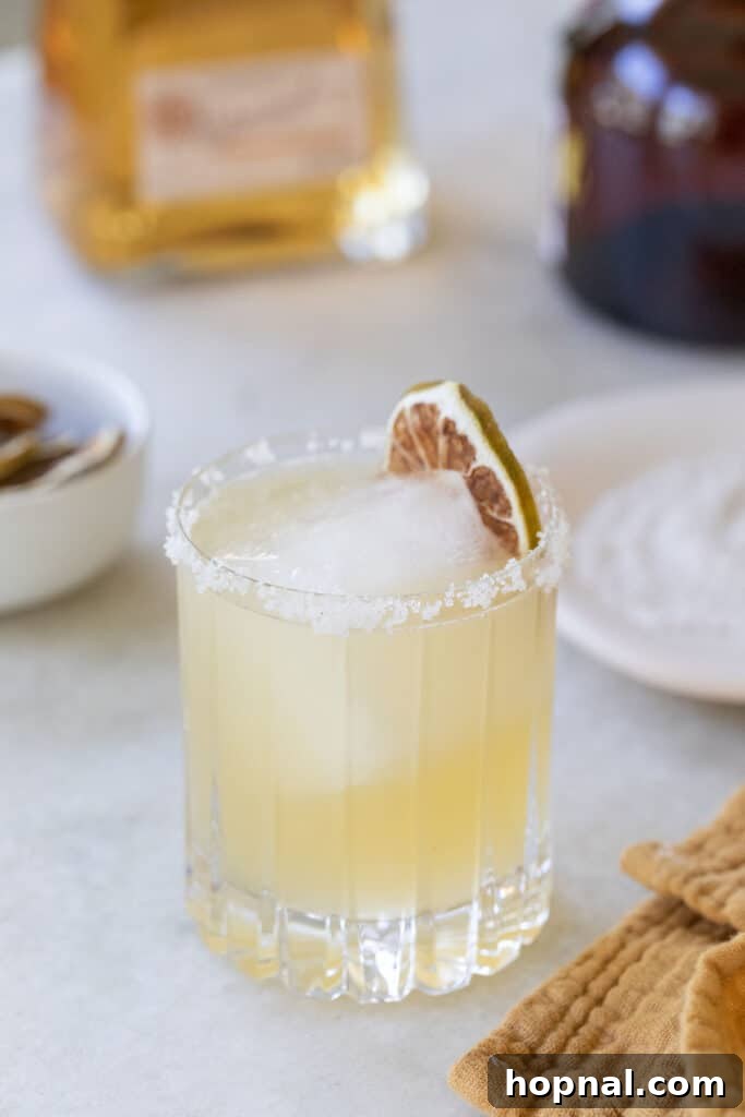 Close-up of a golden margarita with a dried lime garnish and salted rim.