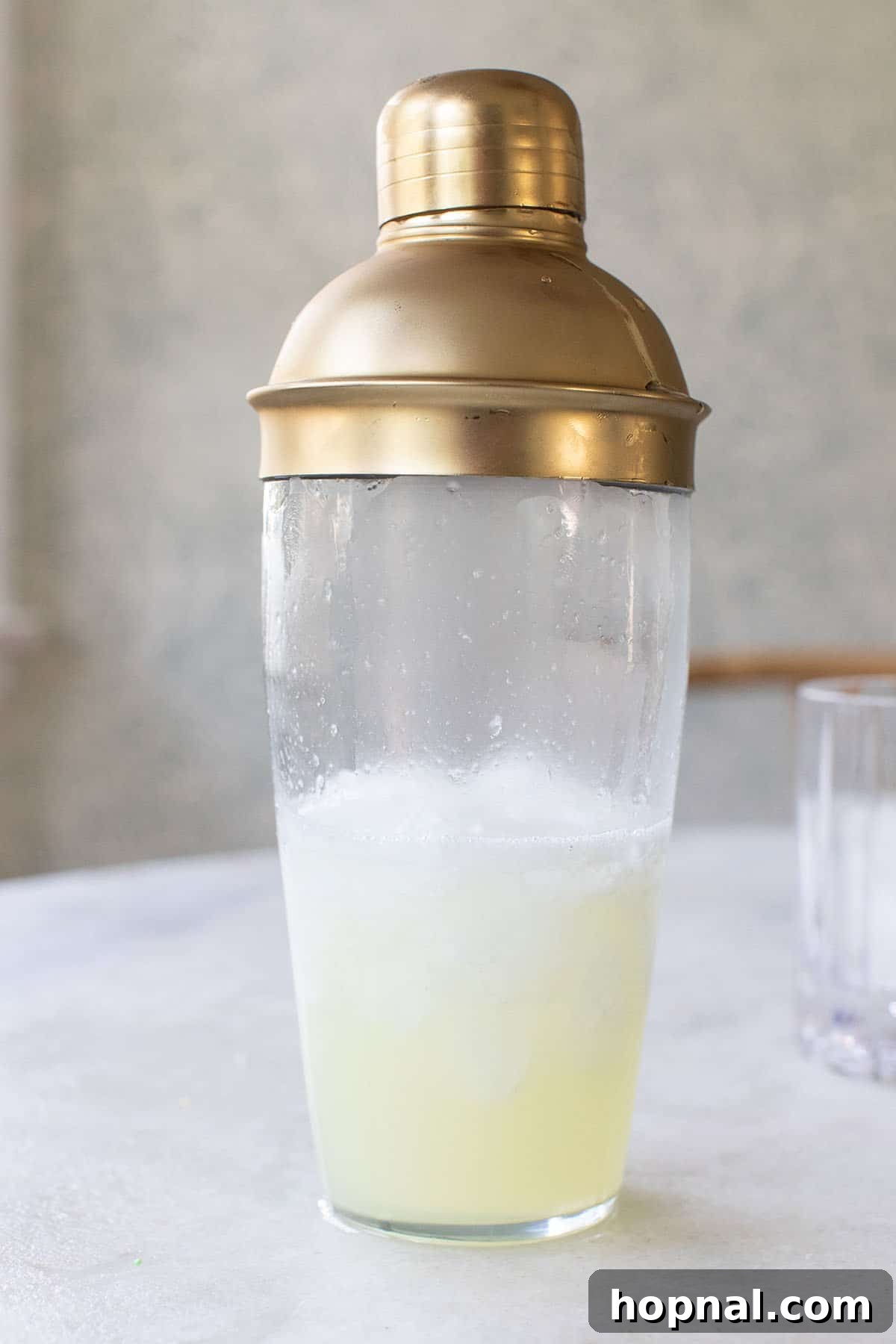 A cocktail shaker filled with the precisely measured ingredients for a Vodka Sour: lemon juice, vodka, egg white, and simple syrup, ready for a vigorous shake.