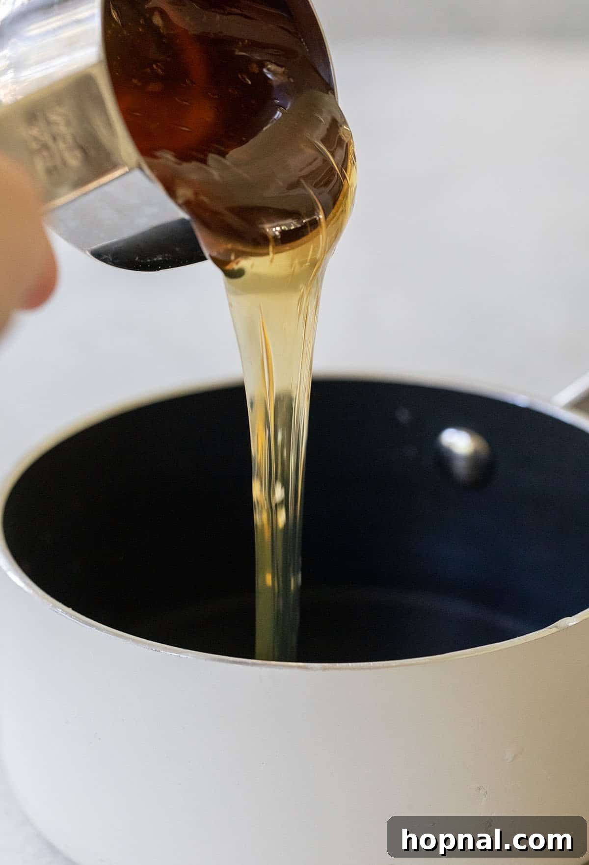 Pouring raw honey into a saucepan to make honey simple syrup.