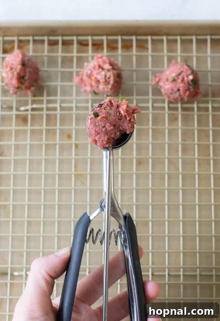 Simple Meatball Bites 6 A small cookie scooper being used to portion out mini meatballs onto a baking sheet.