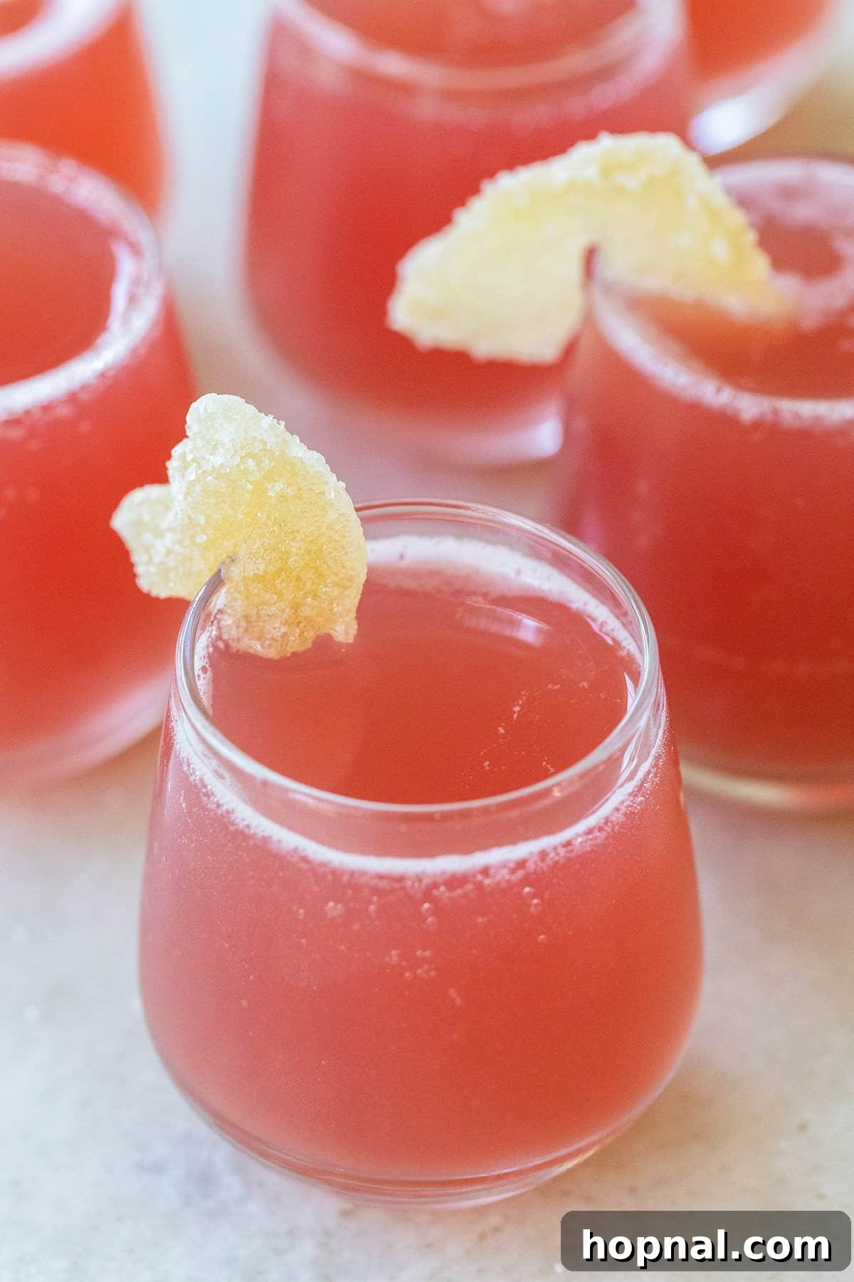 Bright red Jolly Rancher shot in a small glass with candied ginger garnish