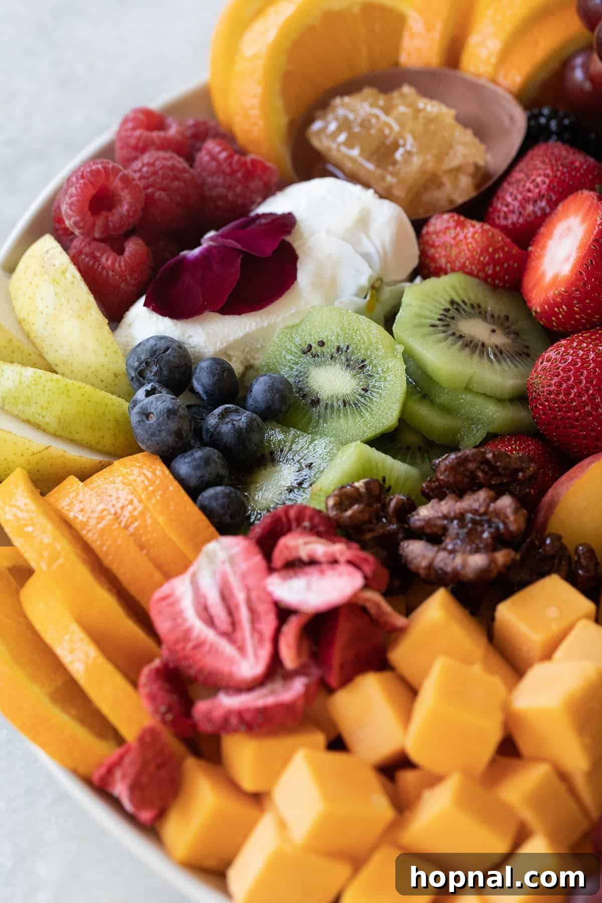 Elegant Cheese and Fruit Board 7 A colorful array of sliced kiwi, strawberries, oranges, peaches, blackberries, and pears arranged for a fruit and cheese platter, with a soft goat cheese.