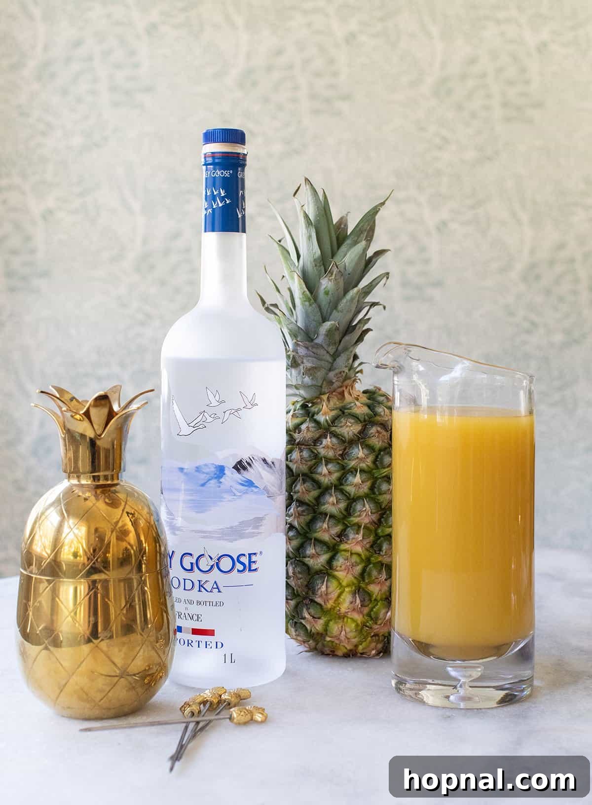 Tropical Pineapple Vodka Elixir 3 Ingredients for a vodka and pineapple juice cocktail laid out on a table: a bottle of vodka, fresh pineapple juice, and fresh limes.
