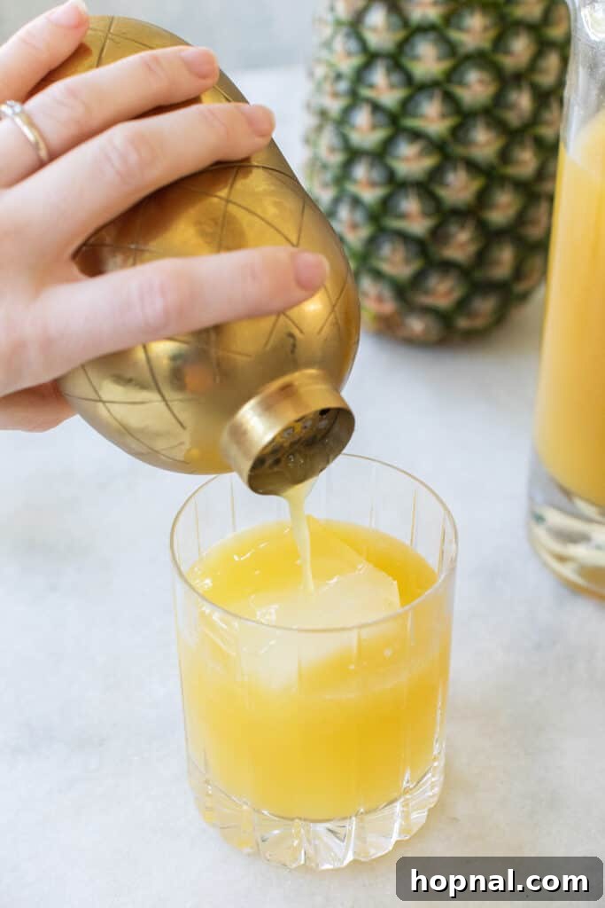 Tropical Pineapple Vodka Elixir 6 A vibrant yellow cocktail being strained from a shaker into a glass filled with fresh ice.