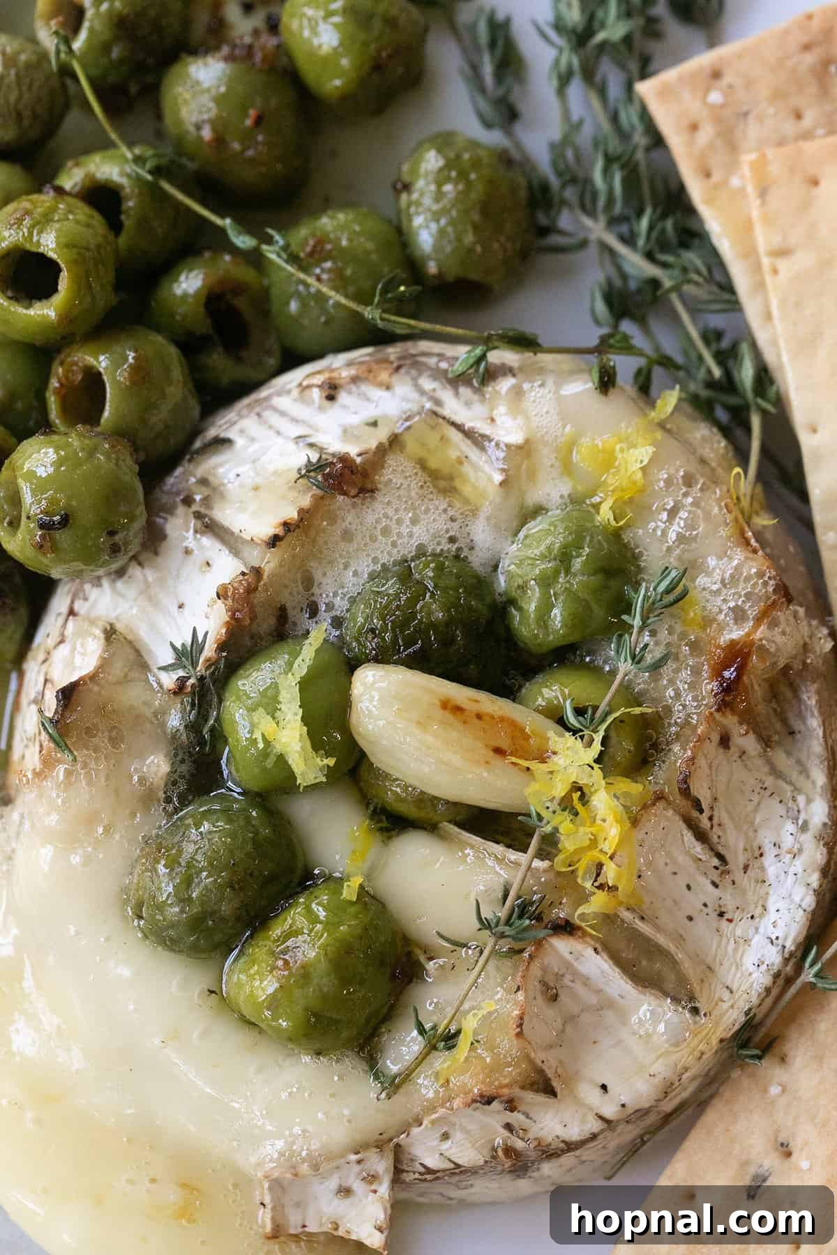Effortless Baked Brie 2 Golden baked brie with a generous topping of vibrant marinated olives and fresh garlic, ready to be served as an appetizer.