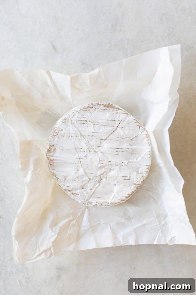 Effortless Baked Brie 3 A perfectly round wheel of brie cheese resting on a sheet of parchment paper, ready for preparation.