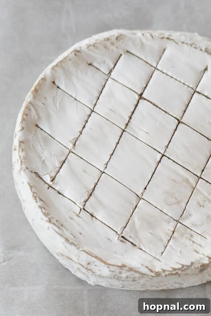 Effortless Baked Brie 4 Close-up of a brie cheese wheel with shallow crosshatch cuts on its top rind.