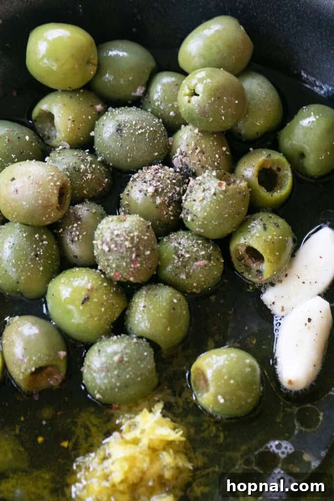Effortless Baked Brie 6 Green olives, garlic, and herbs simmering gently in olive oil in a small skillet for the marinated topping.
