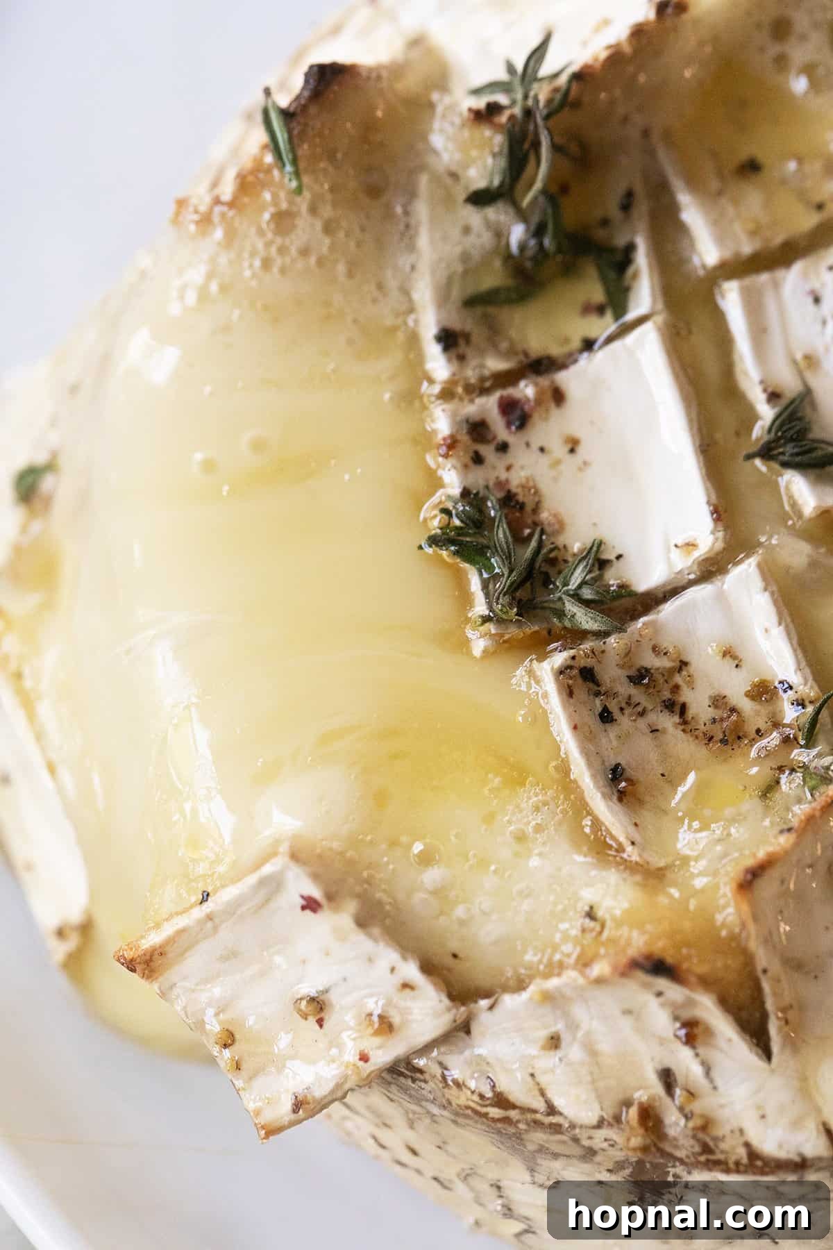 Effortless Baked Brie 7 Close-up of freshly baked, melted brie cheese, showcasing its gooey center, topped with fresh herbs and a hint of pepper.