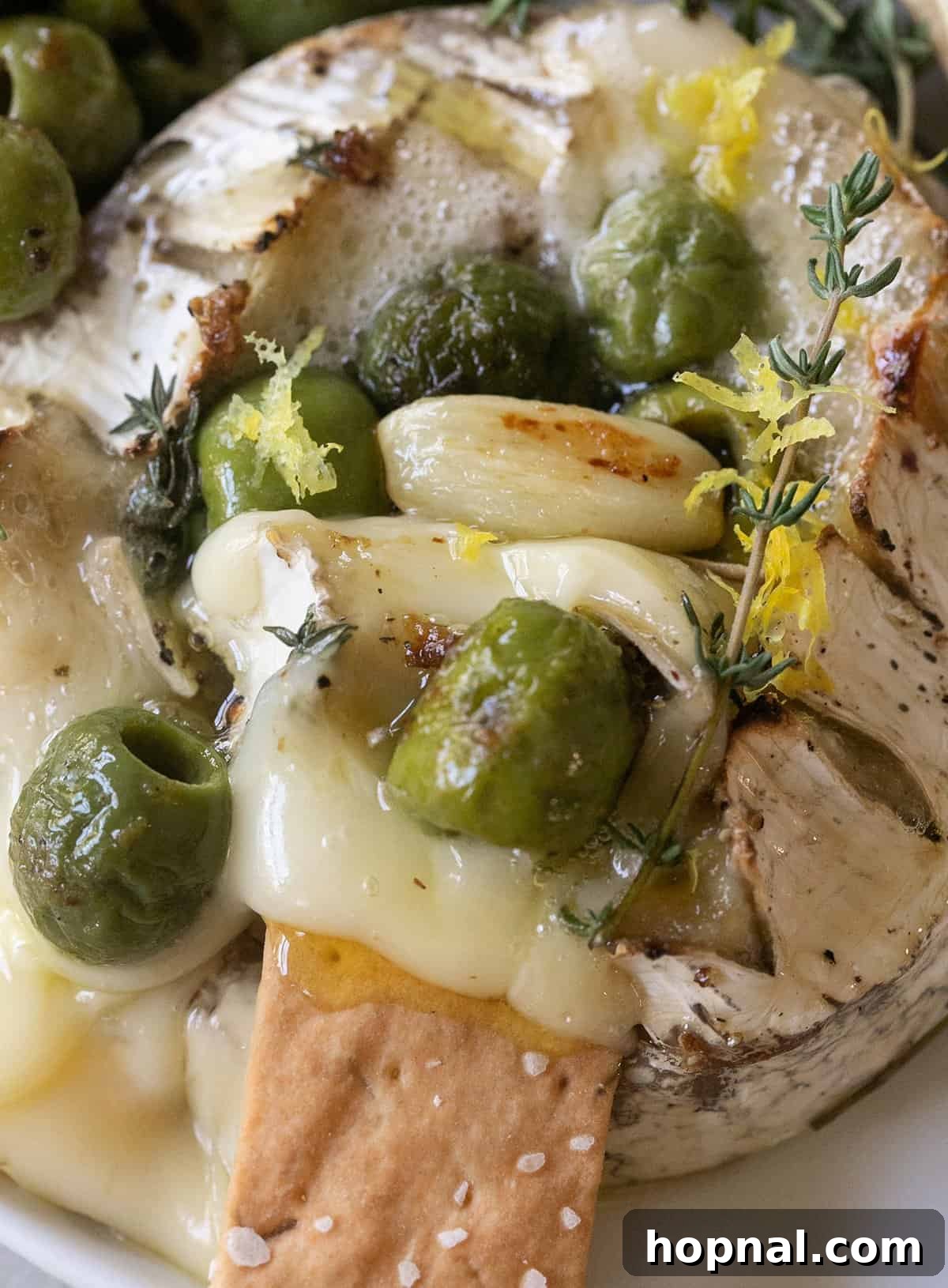 Effortless Baked Brie 8 Generous serving of gooey baked brie with a rich melted center, beautifully topped with savory marinated olives and fresh herbs, ready to be enjoyed.