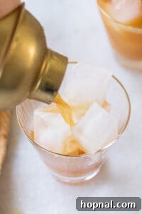 Pouring a well-shaken Brass Monkey cocktail into a glass with fresh ice.