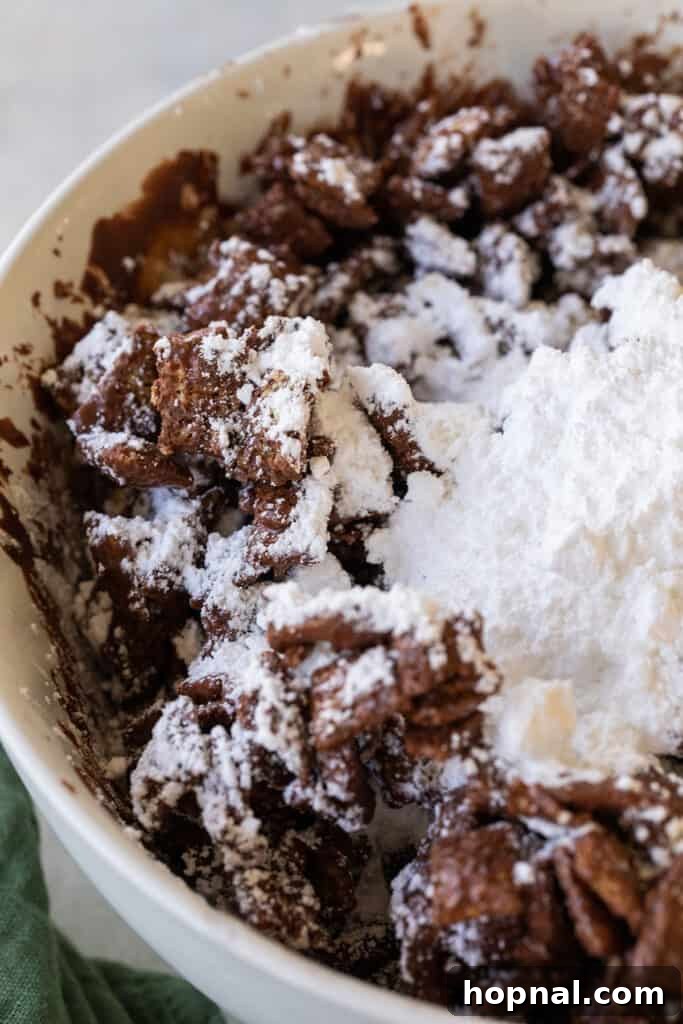 Magic Reindeer Dust 6 Powdered sugar being generously sprinkled over the chocolate-coated cereal mixture, beginning to form the signature snowy layer of the reindeer chow.