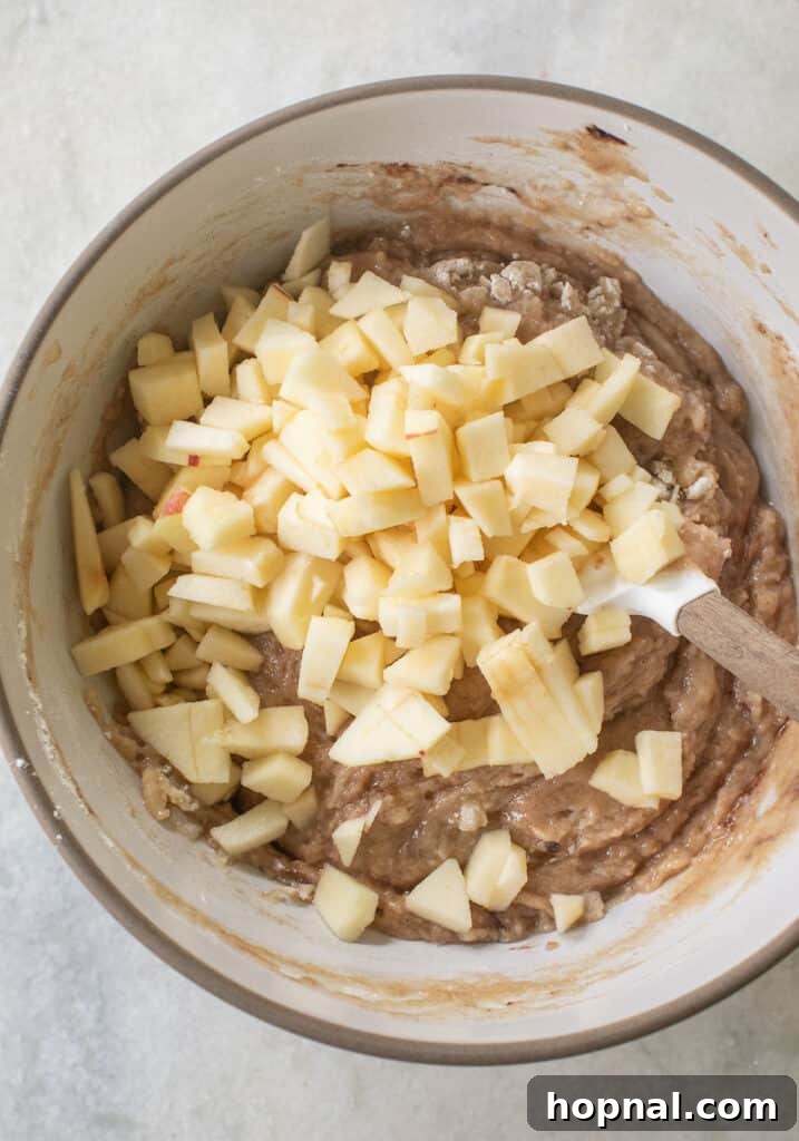 Finely chopped fresh apples being gently folded into the prepared apple cake batter.