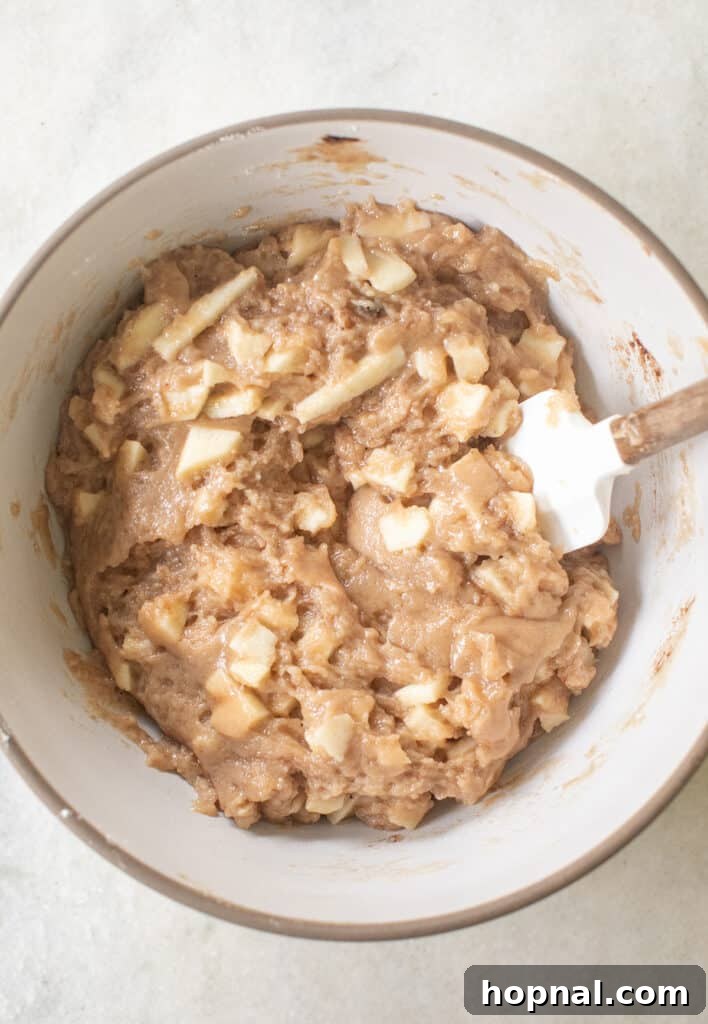 A close-up view of the apple cake batter in a mixing bowl, showcasing visible chunks of fresh apples folded throughout.
