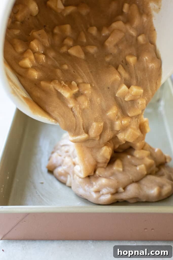 The apple cake batter being poured smoothly into a well-greased and floured cake pan, ready for baking.