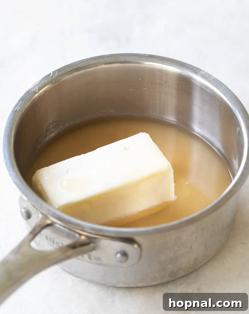 A small saucepan on the stovetop, containing melting butter and apple cider, beginning to simmer for the apple cider glaze.