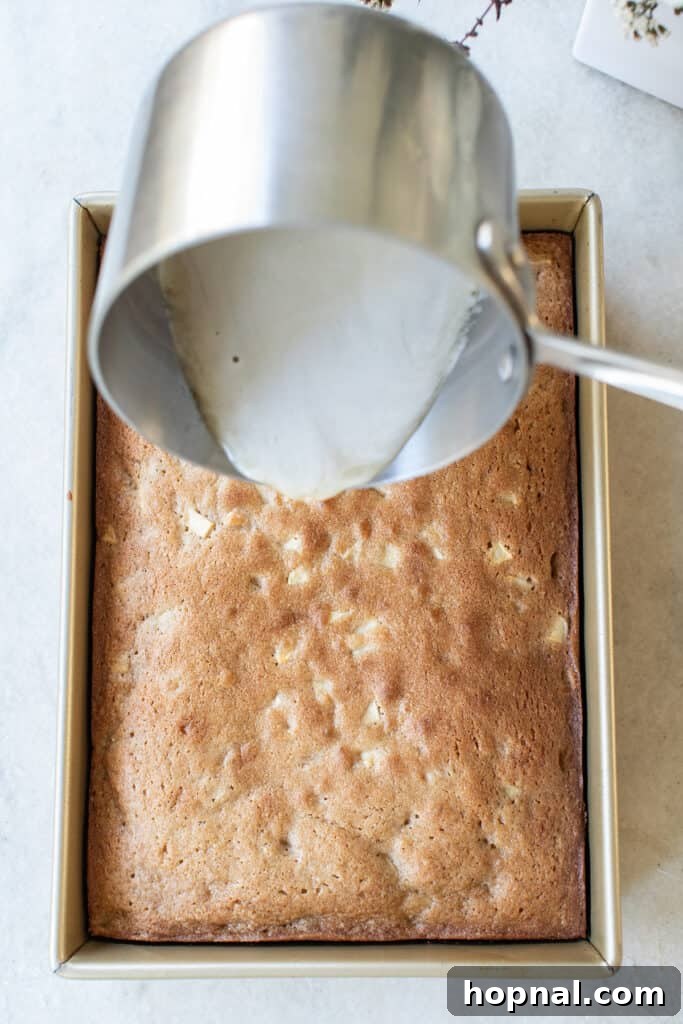 A warm, freshly baked old-fashioned apple cake with the buttery apple cider glaze being generously poured over its surface, creating a glistening finish.