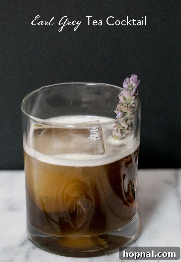 An Earl Grey cocktail with recipe title in text overlay, garnished with a lemon slice and lavender sprig.