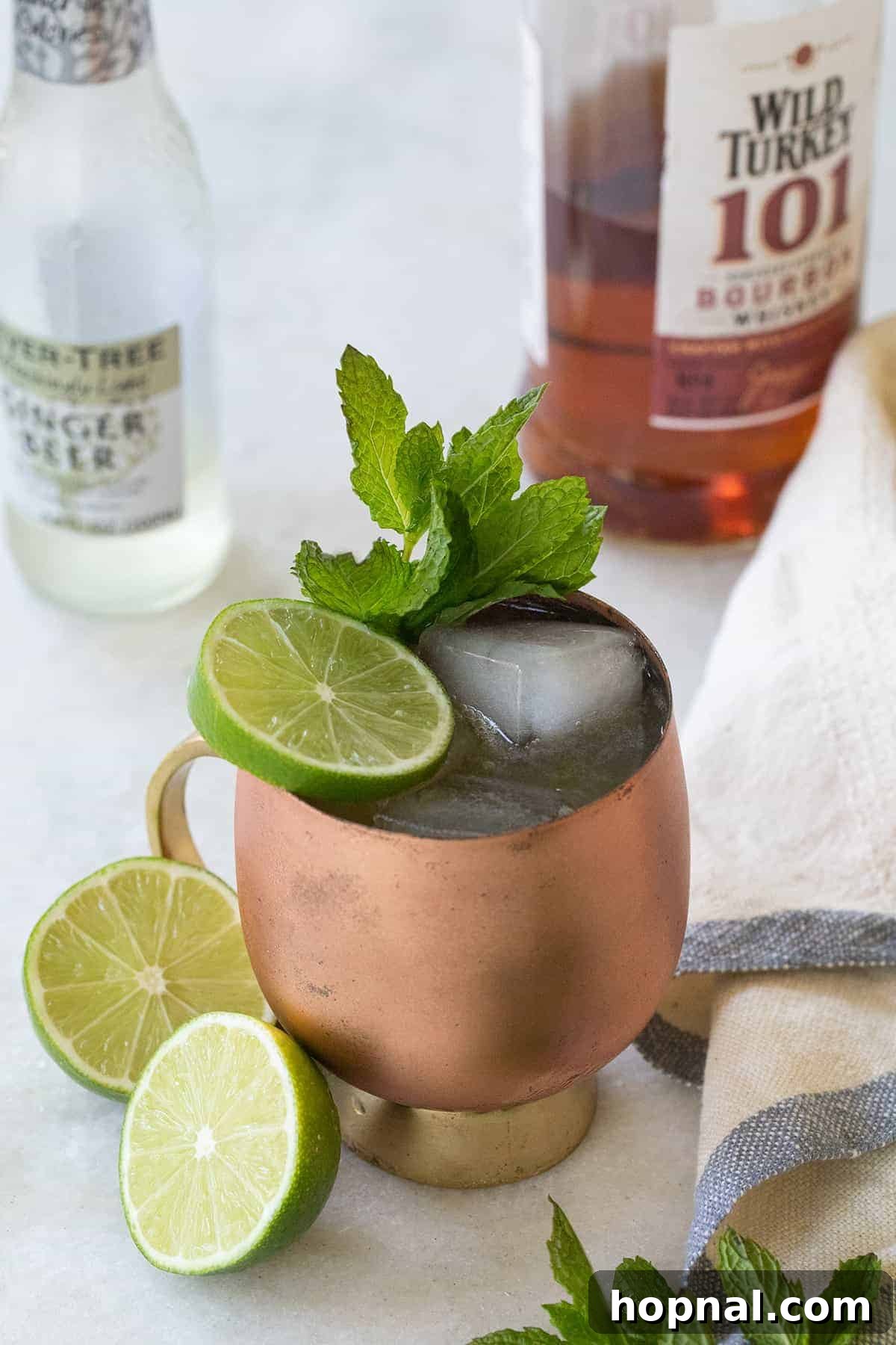 A frosty Kentucky Mule cocktail in a copper mug, garnished with a lime wedge and fresh mint sprig, resting on a marble table.