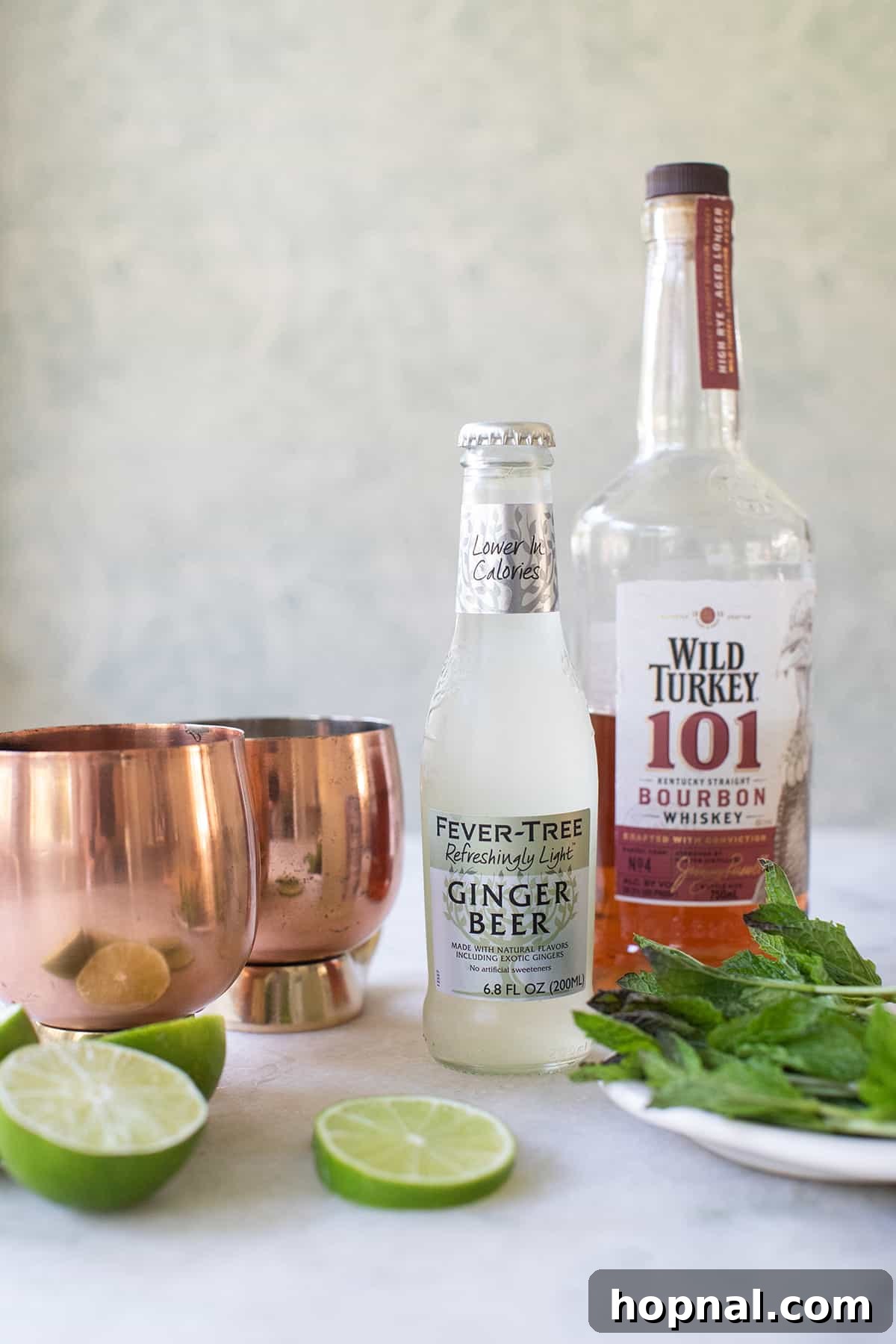 Essential ingredients for a Kentucky Mule: a bottle of bourbon, a can of ginger beer, fresh limes, and an iconic copper mug.