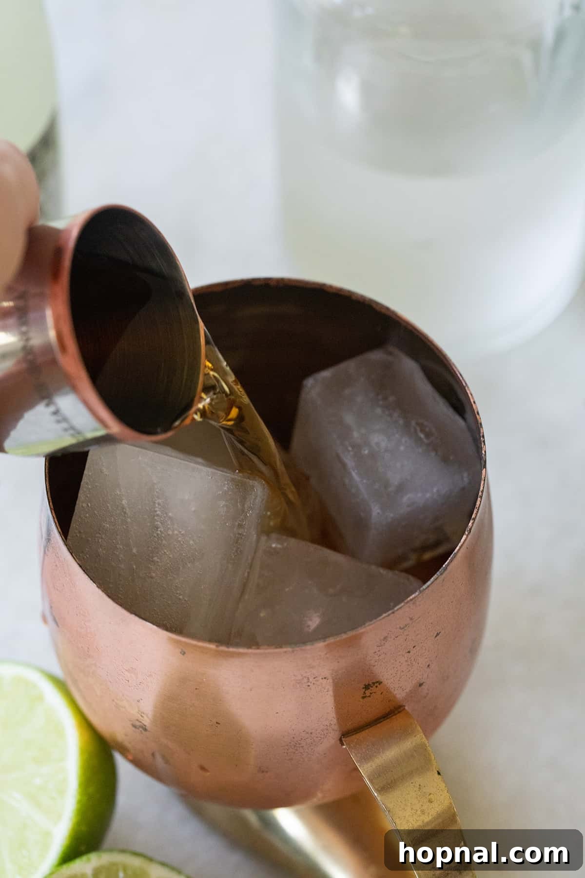 A hand pouring amber bourbon from a bottle into a copper mug filled with ice.