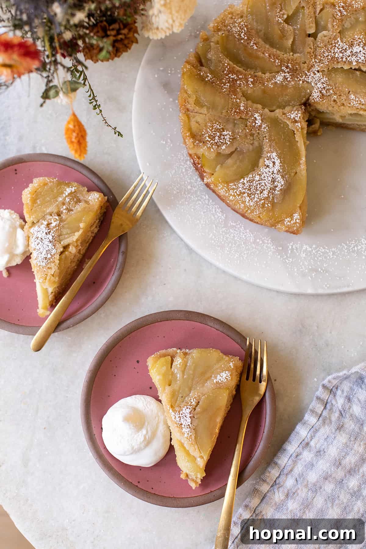 A beautifully caramelized apple upside-down cake on a delicate pink plate, garnished with a dollop of fresh whipped cream and a hint of spice. This fall dessert is moist, tender, and bursting with apple flavor.