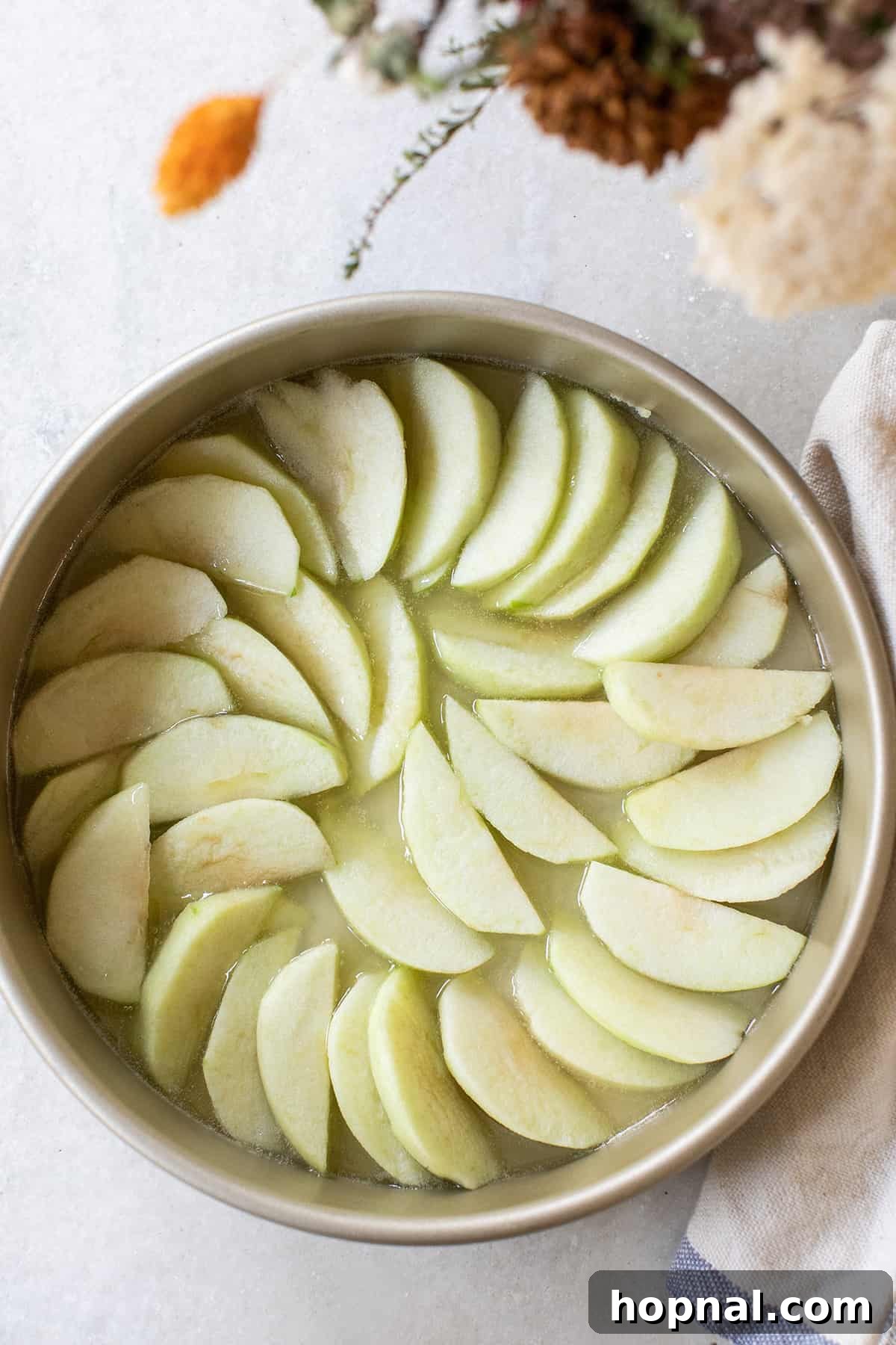 Perfectly arranged, thinly sliced apples creating a beautiful, intricate pattern at the bottom of a round cake tin, ready for the cake batter. This careful arrangement ensures a stunning caramelized topping.