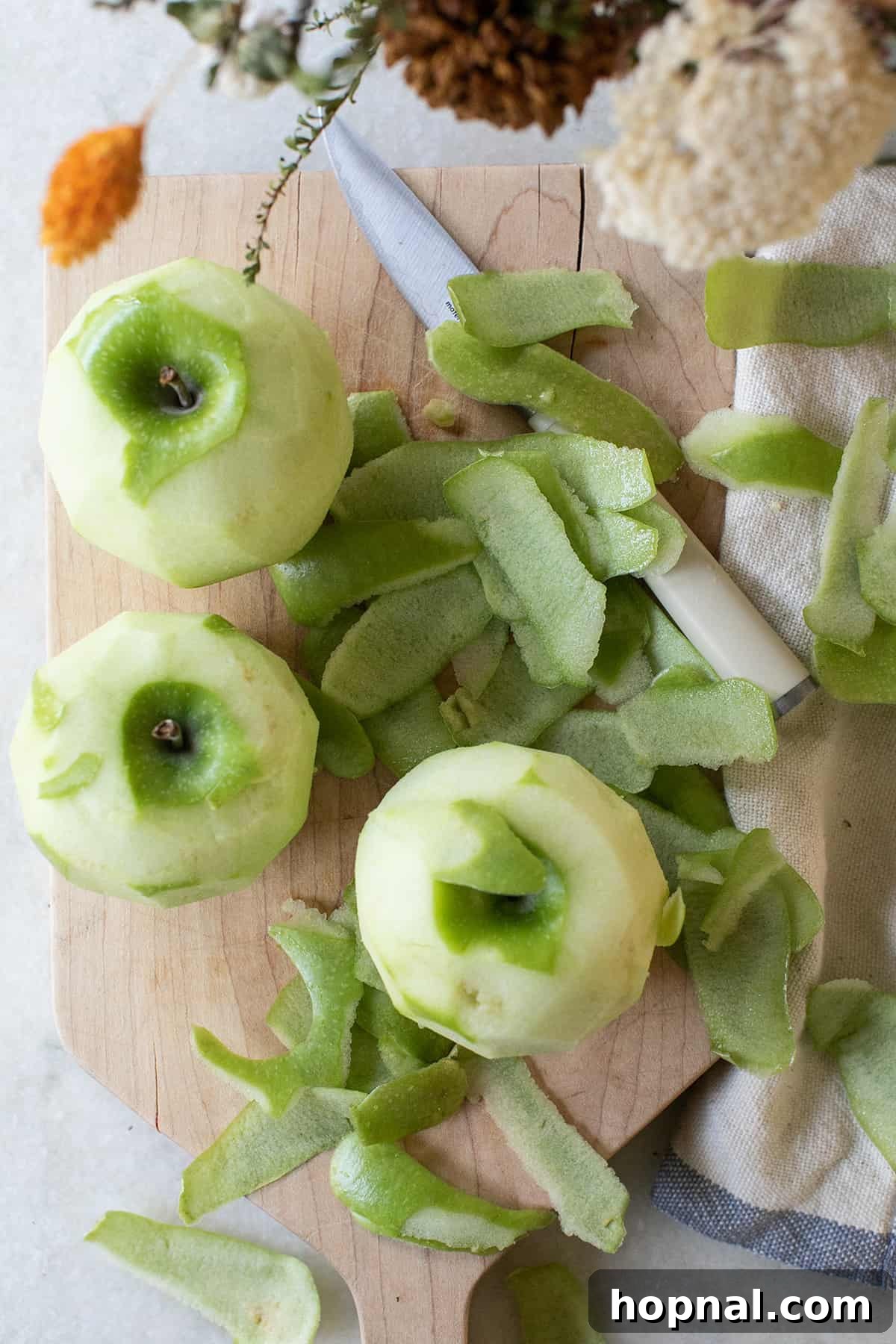 Freshly peeled Granny Smith apples, ready for coring and slicing, resting on a wooden cutting board. Their bright green skin has been removed, revealing the crisp, white flesh perfect for baking.