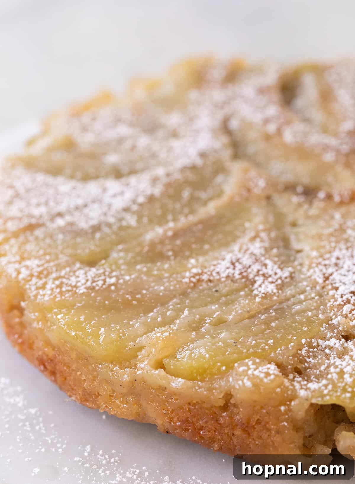 A close-up view of a dense and moist apple upside-down cake slice, revealing the tender caramelized apples and rich cake crumb. The texture is inviting and promises a truly satisfying bite.