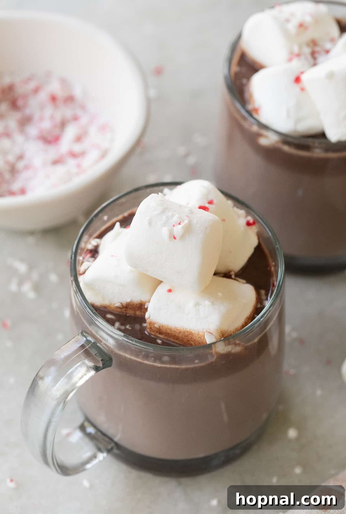 Peppermint mint hot chocolate in a clear mug with marshmallows and crushed candy canes.