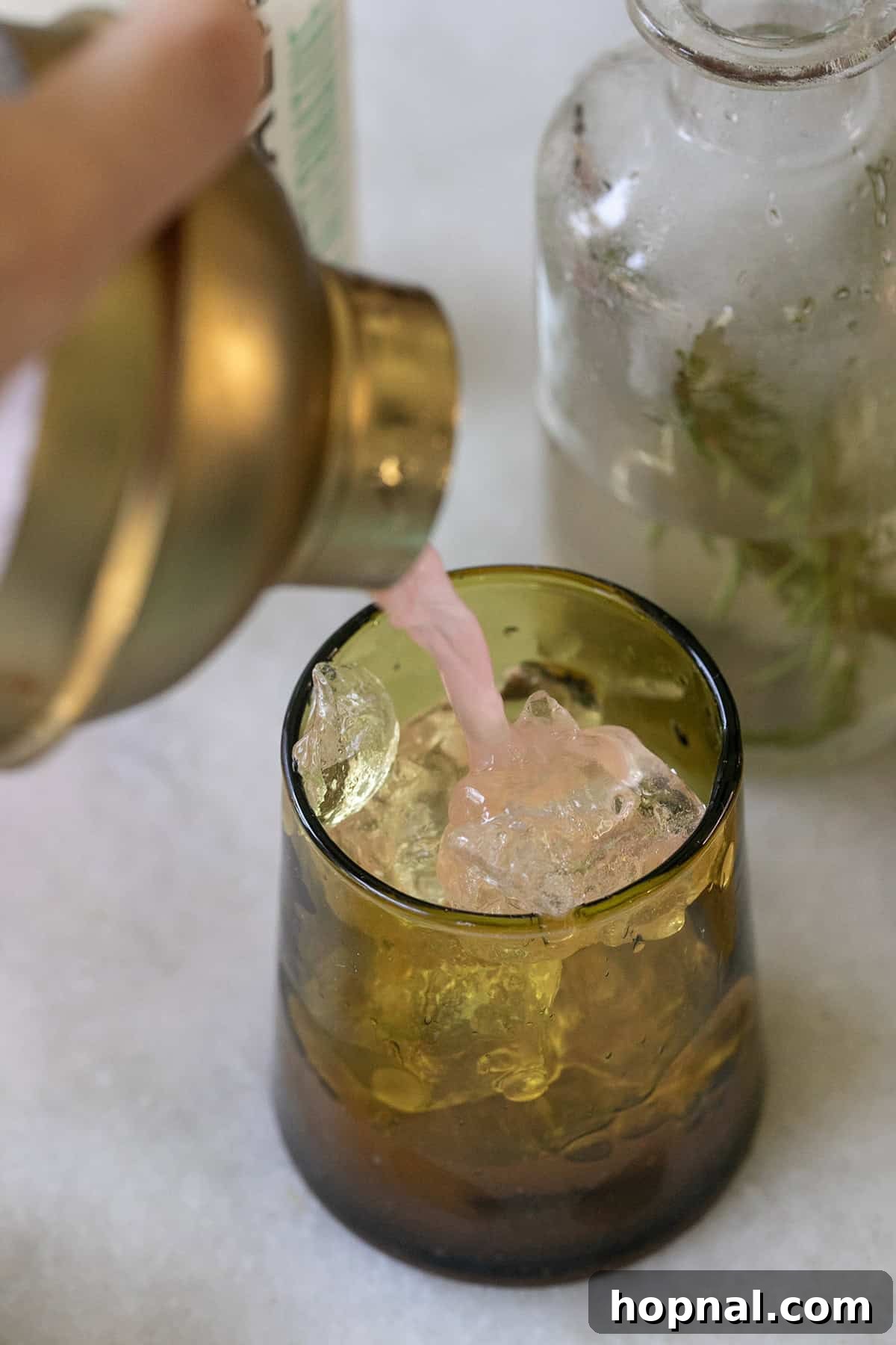 Pouring an apple cider mocktail into a green glass filled with ice.