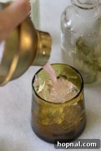 Pouring an apple cider mocktail into a green glass filled with ice.