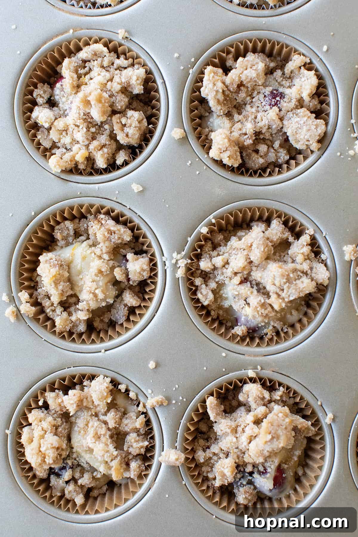 A vibrant close-up of unbaked muffin batter in a cupcake tin, generously adorned with a rich streusel topping, showcasing the raw beauty before baking.