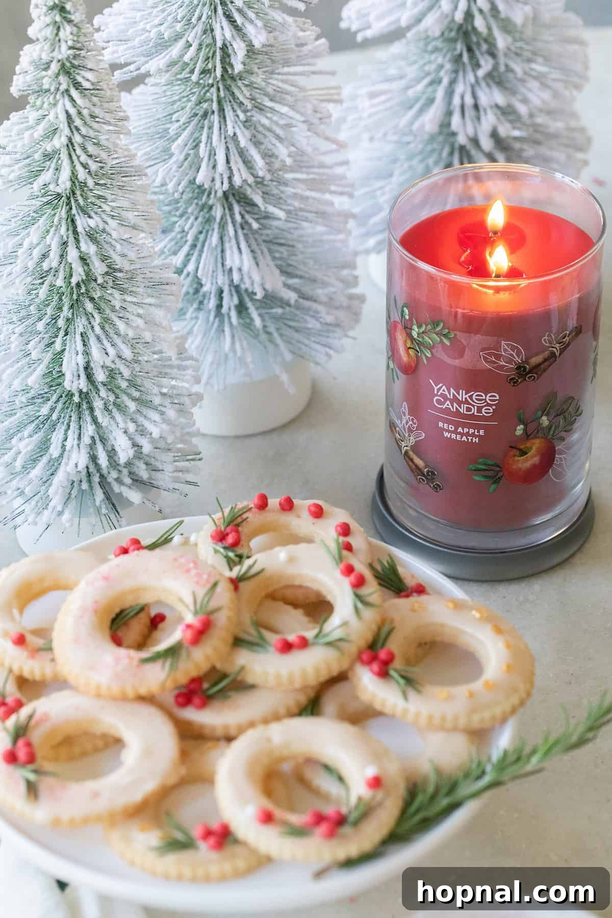 A beautifully arranged platter of freshly baked Christmas wreath cookies sitting next to a glowing Yankee Candle, creating a cozy holiday ambiance.