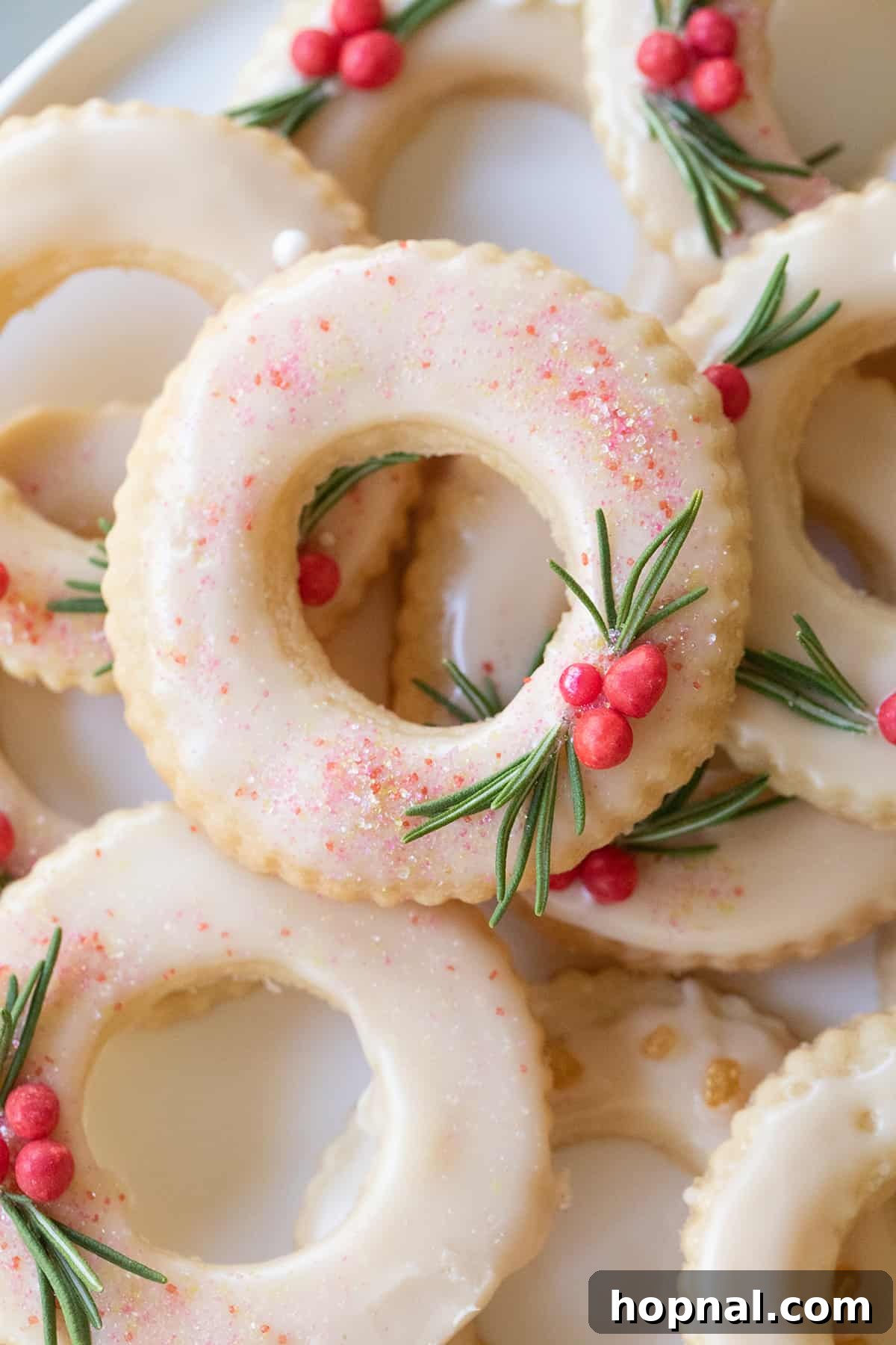A close-up shot of a single butter wreath Christmas cookie, meticulously decorated with green sprinkles and a red candy 'berry'.
